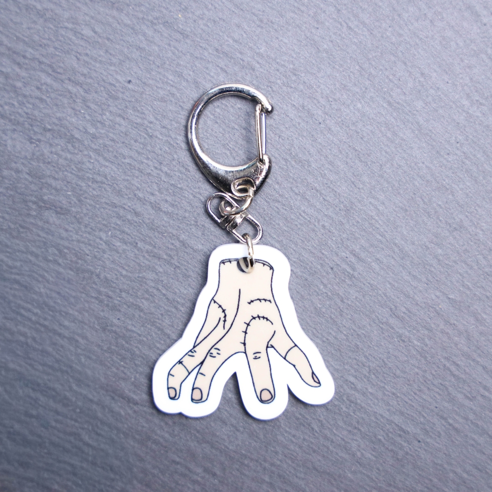 Thing Bag Tag. This bag tag is made with acrylic and heat pressed. Comes with lobster clasp topper that easily hooks to a bag, zippers, and lanyards for fun display and swivels. White backside.