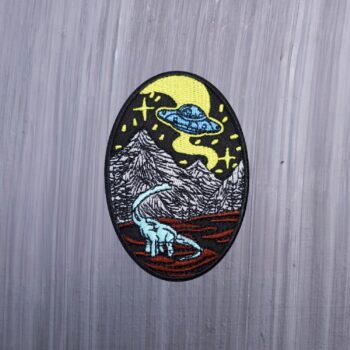 Alien Dinosaur Patch with spaceship, mountains, and dinosaur. Beautifully embroidered design with an adhesive for easy application to your favorite bag or article of clothing.
