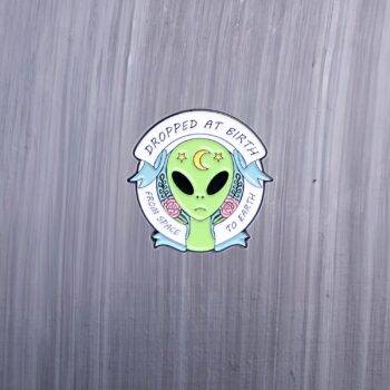 Alien Dropped At Birth From Space to earth enamel pin. Green alien with pink roses and a moon. These enamel pins are made with metal. These enamel pins are colorful, with a black backing.