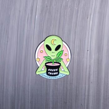 Alien Green Thumb Enamel Pin with plant. These enamel pins are made with metal. These enamel pins are colorful, with a black backing.