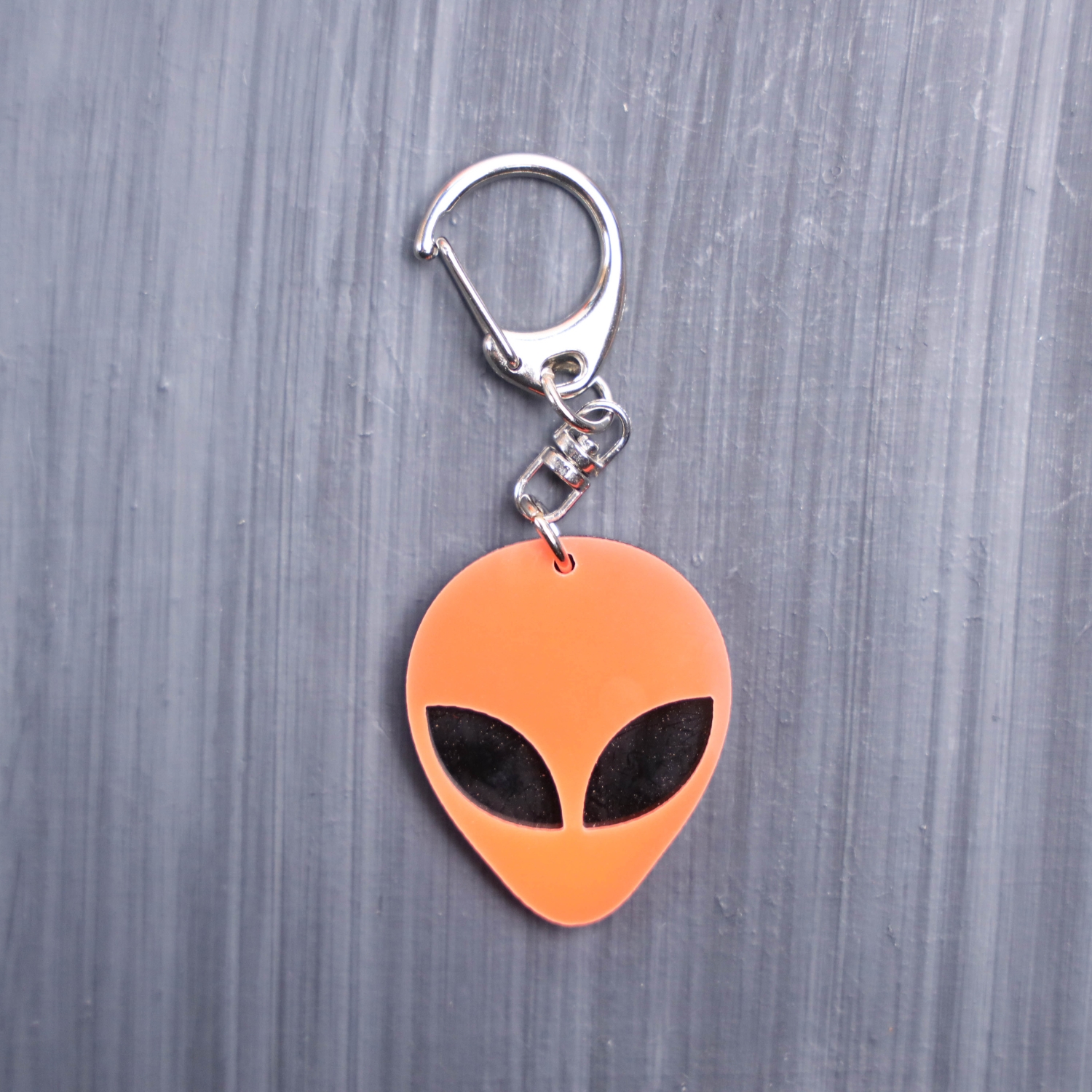 Alien Head Neon Orange Bag Tag with black eyes and black backing. Acrylic designed charm with a swivel lobster snap hook in high quality metal alloy.