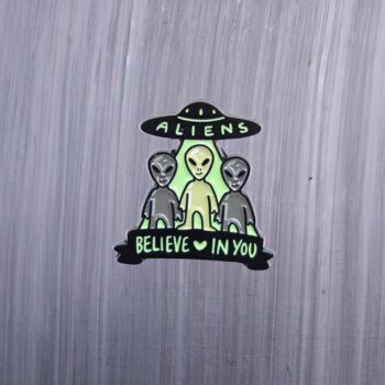 Aliens Believe In You Enamel Pin in black and green. These enamel pins are made with metal. These enamel pins are colorful, with a black backing.