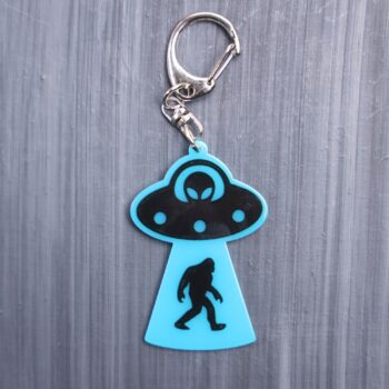 Bigfoot Abduction Neon Blue Bag Tag with black ship and black backing. Acrylic designed charm with a swivel lobster snap hook in high quality metal alloy.
