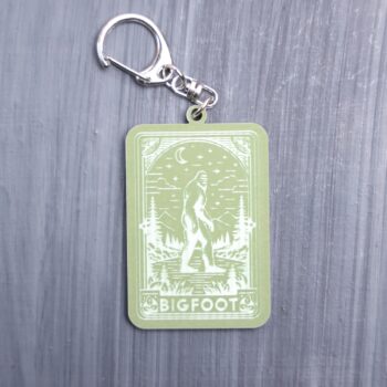 Bigfoot tarot card bag tag in green with trees, moon, and mountains. Acrylic designed charm with a swivel lobster snap hook in high quality metal alloy.