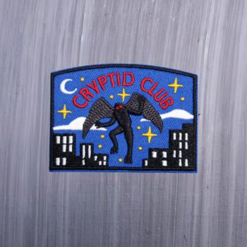 Cryptid Club Mothman Patch with mothman in black and city scene. Beautifully embroidered design with an adhesive for easy application to your favorite bag or article of clothing.