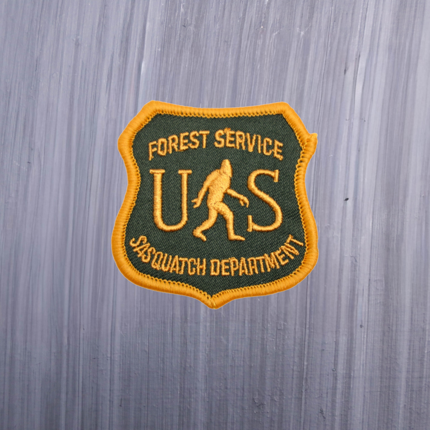 Forest Service Sasquatch Department Patch with a bigfoot on it and US in green and yellow. Beautifully embroidered design with an adhesive for easy application to your favorite bag or article of clothing.