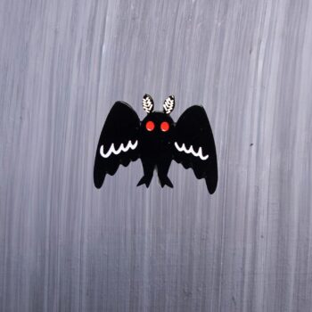 Mothman Big Wings Enamel Pin with black wings wide open and red eyes. These enamel pins are made with metal. These enamel pins are colorful, with a black backing.