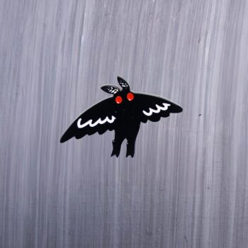 Mothman Flight Enamel Pin with wings in flight, black and white, and with red eyes. These enamel pins are made with metal. These enamel pins are colorful, with a black backing.