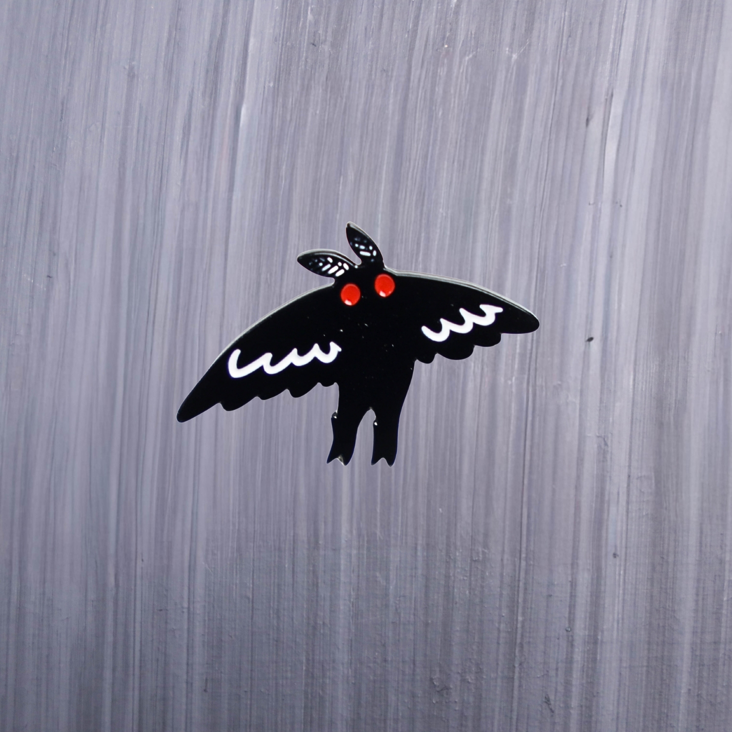 Mothman Flight Enamel Pin with wings in flight, black and white, and with red eyes. These enamel pins are made with metal. These enamel pins are colorful, with a black backing.