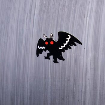 Mothman Walking Enamel Pin with black and white wings and red eyes. These enamel pins are made with metal. These enamel pins are colorful, with a black backing.