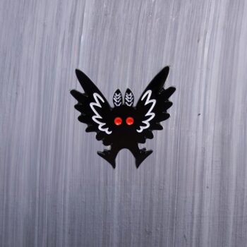 Mothman Wings Up Enamel Pin with black and white wings up and red eyes. These enamel pins are made with metal. These enamel pins are colorful, with a black backing.