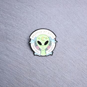Alien Dropped At Birth From Space to earth enamel pin. Green alien with pink roses and a moon. These enamel pins are made with metal. These enamel pins are colorful, with a black backing.
