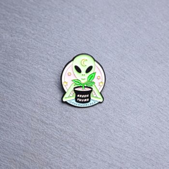 Alien Green Thumb Enamel Pin with plant. These enamel pins are made with metal. These enamel pins are colorful, with a black backing.