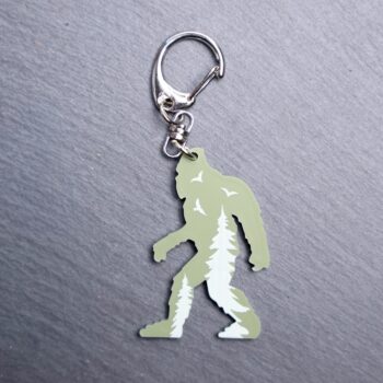 Bigfoot Forest Engraved Green Bag Tag with trees and birds. Acrylic designed charm with a swivel lobster snap hook in high quality metal alloy.