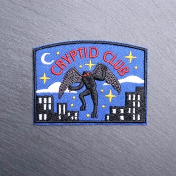 Cryptid Club Mothman Patch with mothman in black and city scene. Beautifully embroidered design with an adhesive for easy application to your favorite bag or article of clothing.
