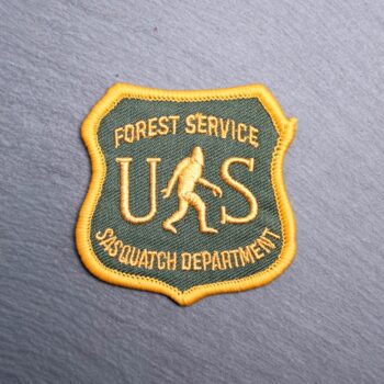 Forest Service Sasquatch Department Patch with a bigfoot on it and US in green and yellow. Beautifully embroidered design with an adhesive for easy application to your favorite bag or article of clothing.