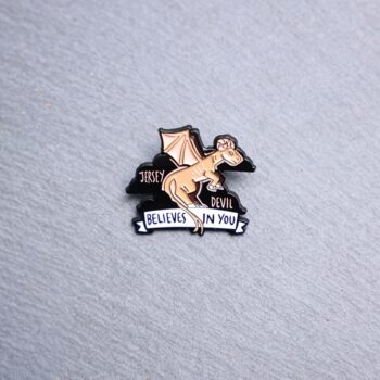 Jersey Devil Believes In You Enamel Pin in brown, pink, and black. These enamel pins are made with metal. These enamel pins are colorful, with a black backing.