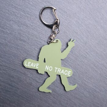 Leave No Trace Bigfoot Bag Tag in green with snow board. Acrylic designed charm with a swivel lobster snap hook in high quality metal alloy.
