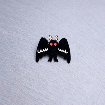 Mothman Big Wings Enamel Pin with black wings wide open and red eyes. These enamel pins are made with metal. These enamel pins are colorful, with a black backing.