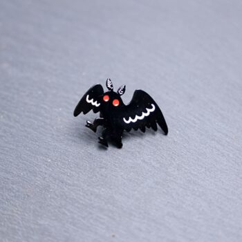 Mothman Walking Enamel Pin with black and white wings and red eyes. These enamel pins are made with metal. These enamel pins are colorful, with a black backing.