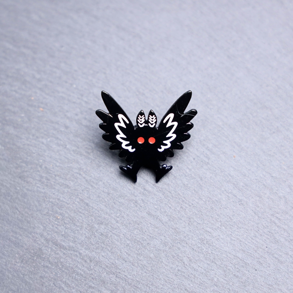 Mothman Wings Up Enamel Pin with black and white wings up and red eyes. These enamel pins are made with metal. These enamel pins are colorful, with a black backing.