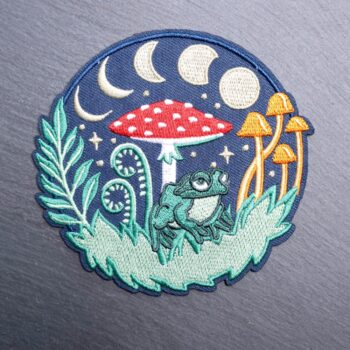 Forest Frog patch with a frog, mushrooms, and moons. Beautifully embroidered design with an adhesive for easy application to your favorite bag or article of clothing.