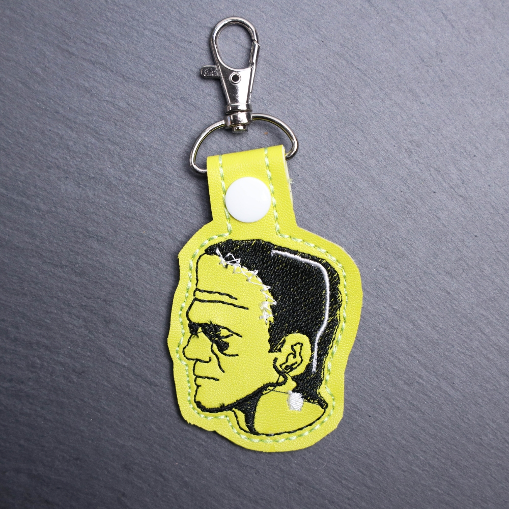 Frankenstein Snap Bag Tag. This bag tag is made with faux vinyl and embroidered. Comes with lobster clasp topper that easily hooks to a bag, zippers