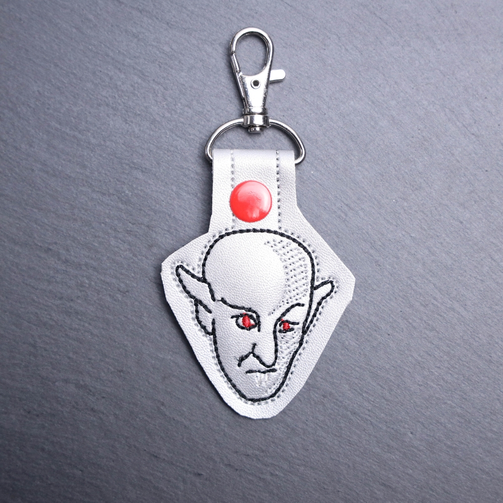 Nosferatu Snap Bag Tag. This bag tag is made with faux vinyl and embroidered. Comes with lobster clasp topper that easily hooks to a bag, zippers