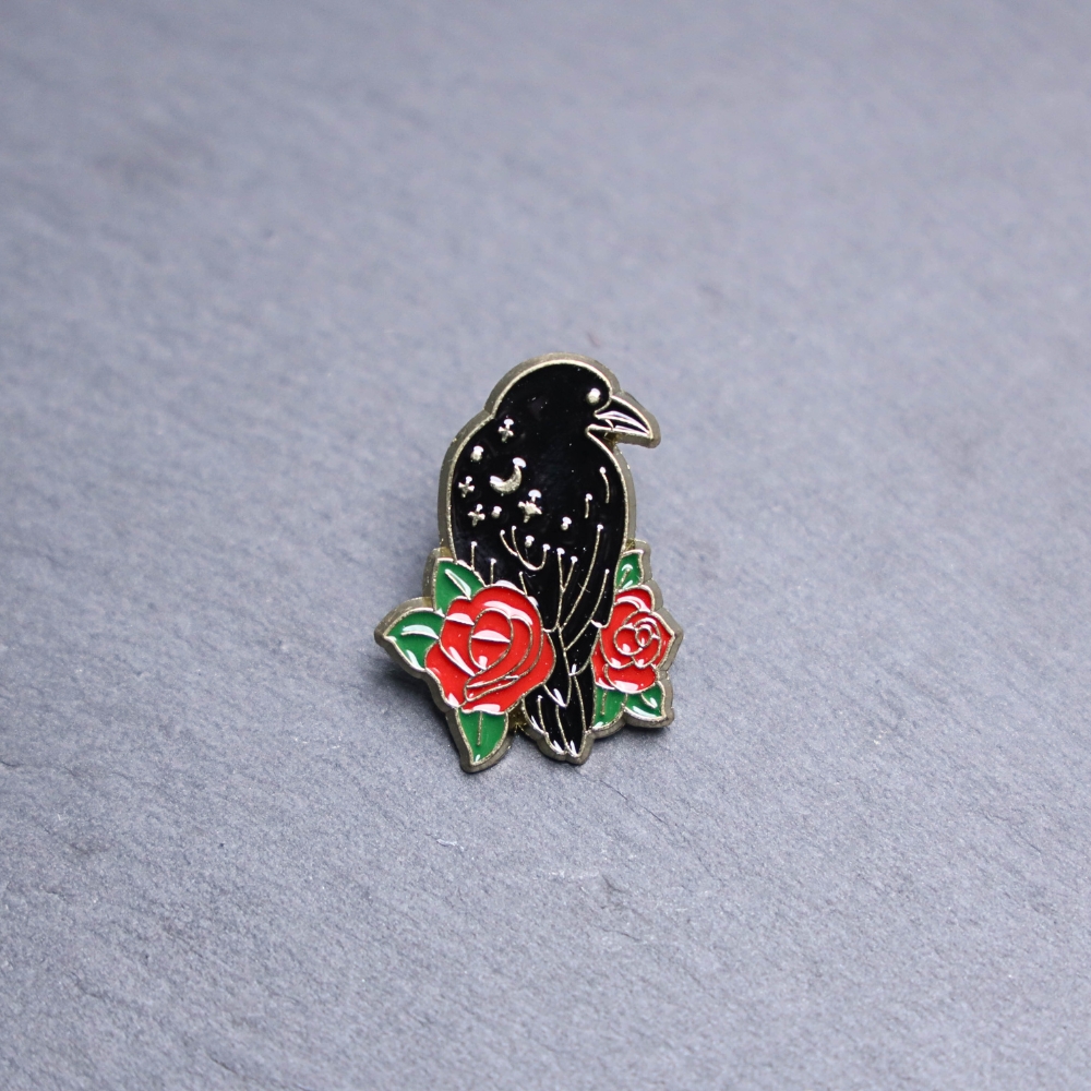 Raven Rose Enamel Pin with black raven and roses. These enamel pins are made with metal. These enamel pins are colorful, with a black backing.