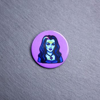 Lily Munster Button. These buttons are made with photo paper, metal round, and metal backing. These buttons are vibrant and fun to use on bags or vests.
