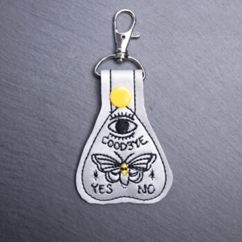 Planchette Snap Bag Tag. This bag tag is made with faux vinyl and embroidered. Comes with lobster clasp topper that easily hooks to a bag, zippers