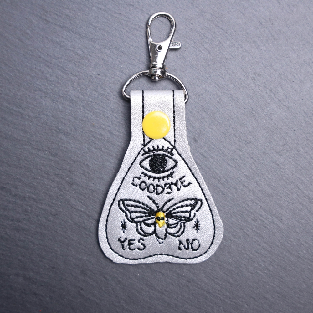 Planchette Snap Bag Tag. This bag tag is made with faux vinyl and embroidered. Comes with lobster clasp topper that easily hooks to a bag, zippers