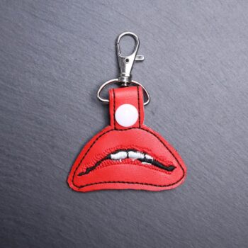 RHPS Lips Snap Bag Tag. This bag tag is made with faux vinyl and embroidered. Comes with lobster clasp topper that easily hooks to a bag, zippers