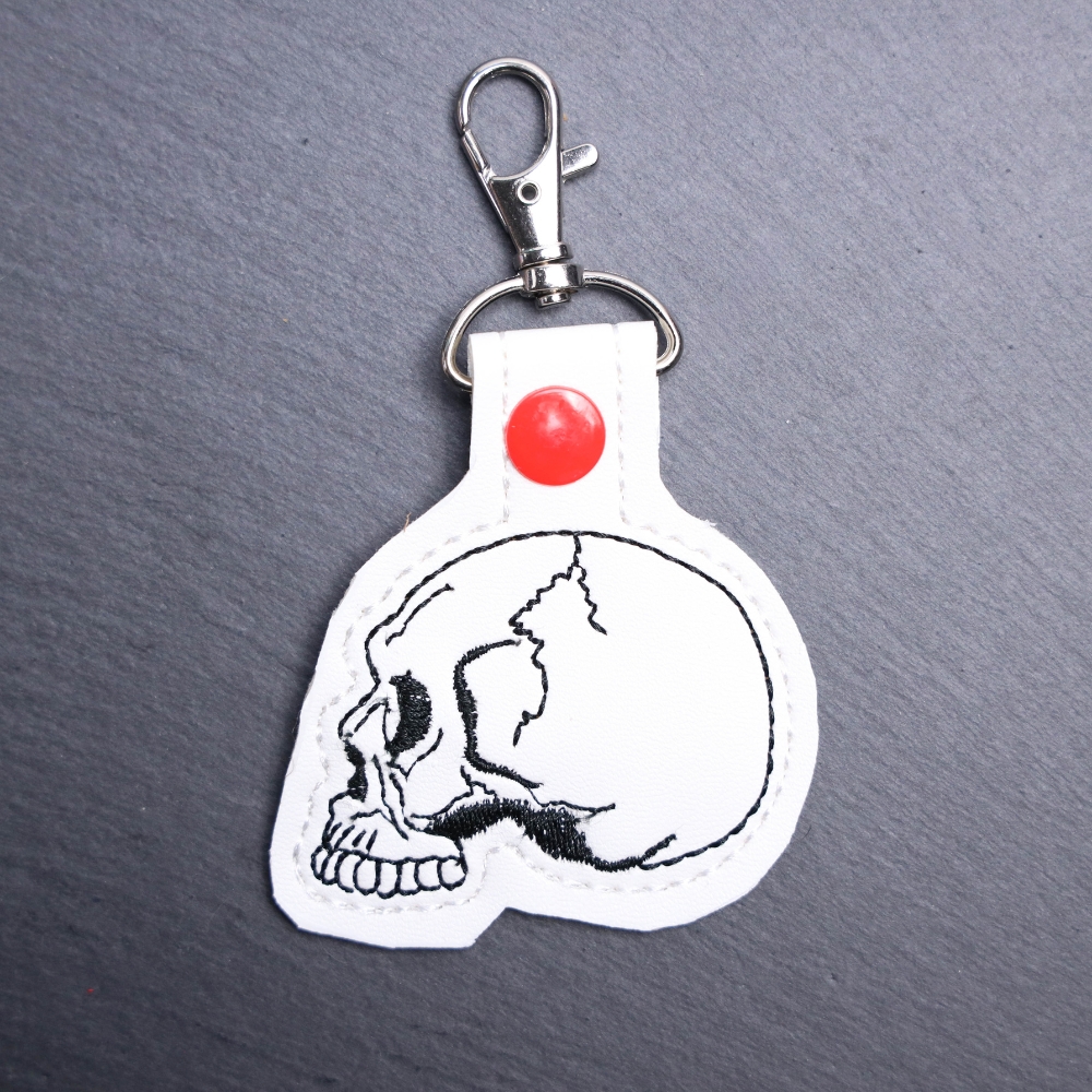 Skull Snap Bag Tag. This bag tag is made with faux vinyl and embroidered. Comes with lobster clasp topper that easily hooks to a bag, zippers