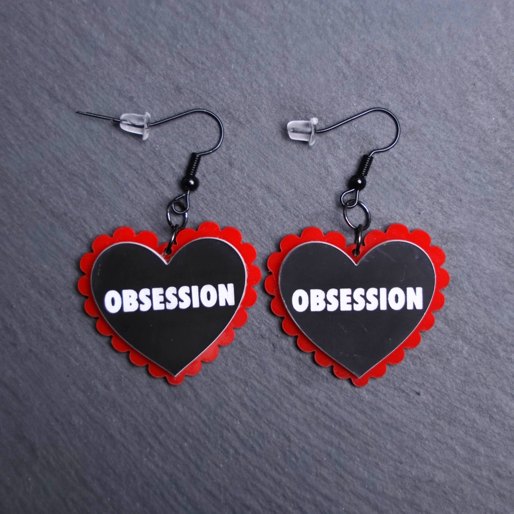 Obsession Pillow Earrings that are white, black and red. These earrings are made with engraved acrylic. Comes with black hooks that is nickel free.