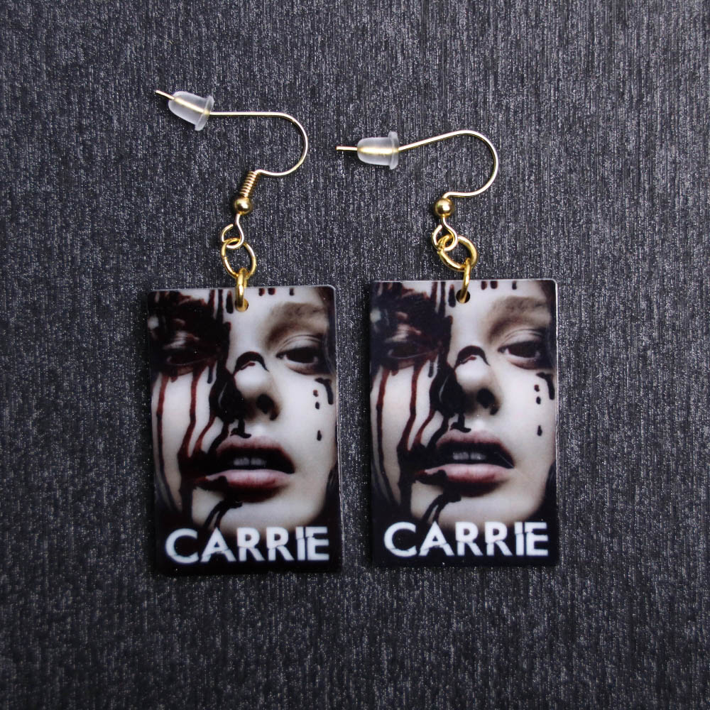 Carrie Poster Earrings. These earrings are made with acrylic and hand heat pressed. Comes with 18k plated gold hooks that is nickel free. Slightly distressed and reflects in light.